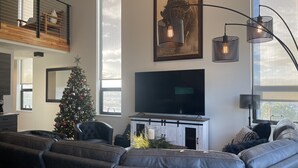 A modern living room with a large flat-screen TV, a Christmas tree, leather sofas, and a fireplace. - MT Luxury! (Bozeman)