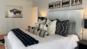 A bedroom with a large bed, multiple pillows, a headboard, and wall art. - MT Luxury! (Bozeman)