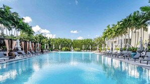 Ein großer, klarer Pool mit Liegestühlen und Sonnenschirmen, umgeben von Palmen und einem Gebäude im modernen Stil.