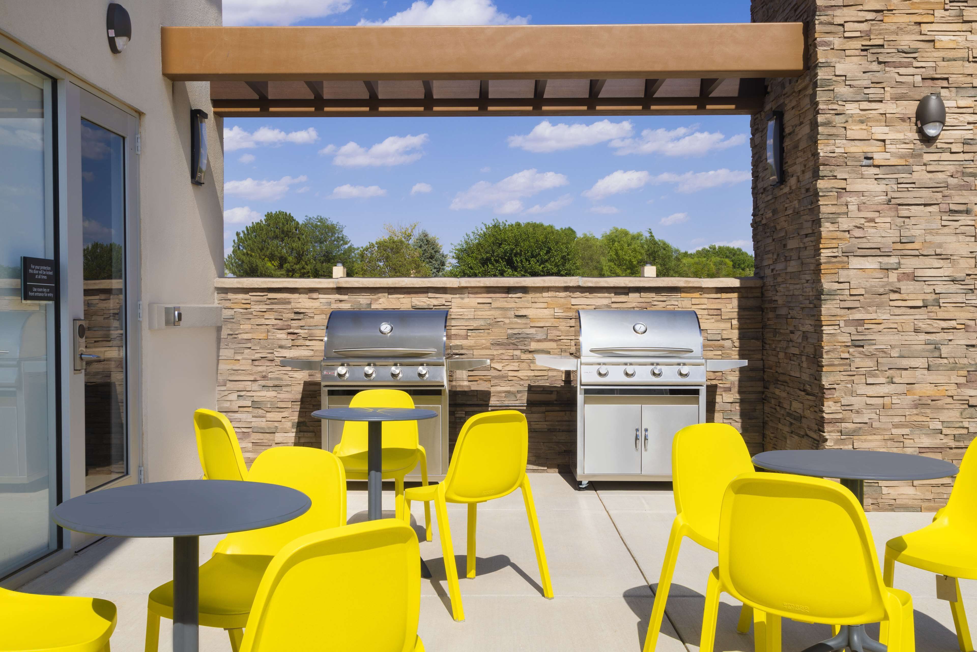 An outdoor patio with yellow chairs and tables, a stone wall, and a grill area.