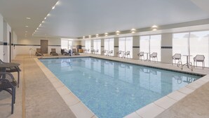 An indoor swimming pool with clear blue water, surrounded by lounge chairs and tables. - Home2 Suites by Hilton Clovis (Clovis)