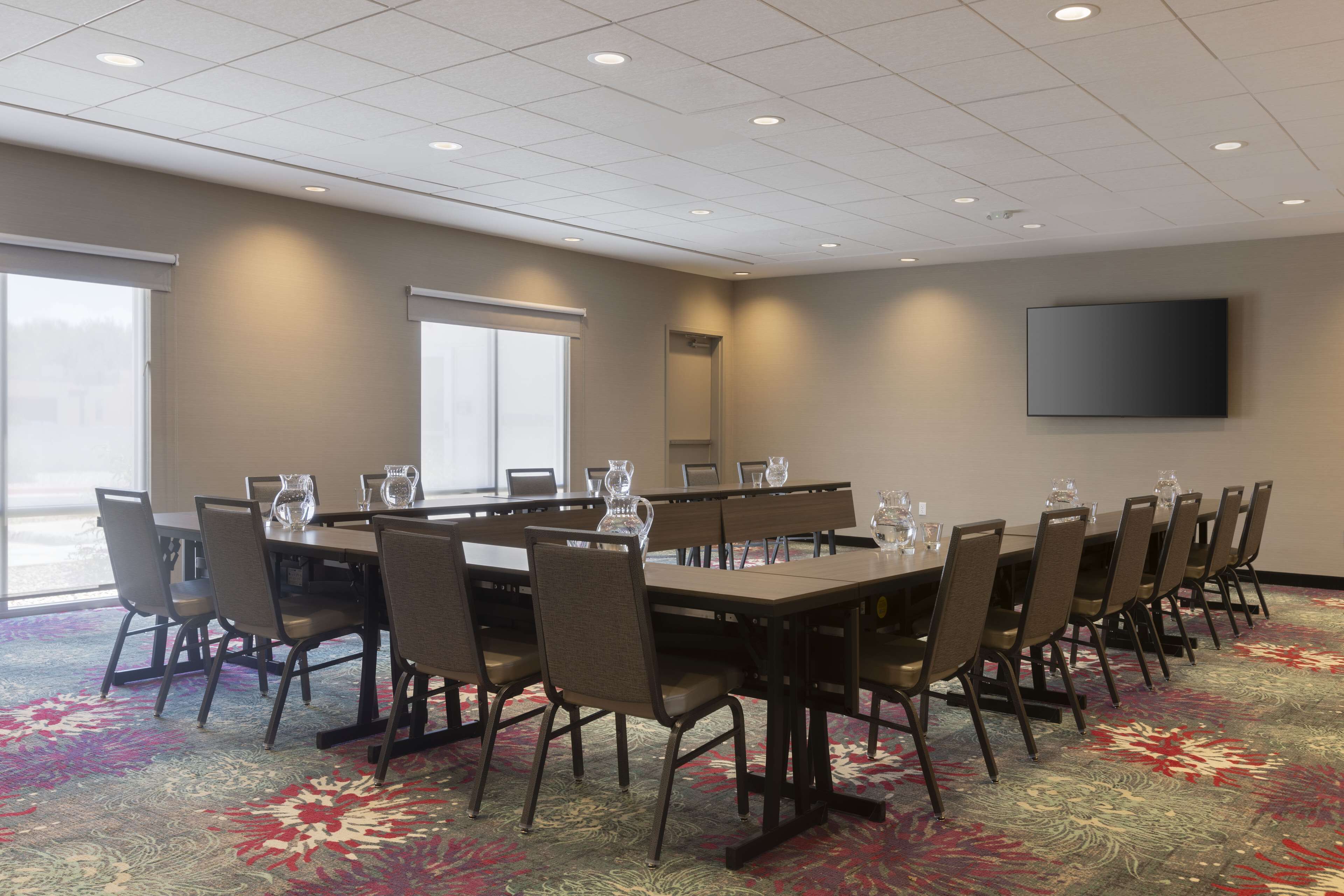 Une salle de conférence avec une longue table, des chaises et un téléviseur à écran plat fixé au mur.