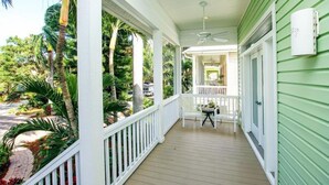 A covered porch with white railings, a ceiling fan, and a view of a lush garden with palm trees. - All Seasons Villa (Captiva)