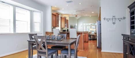 A spacious kitchen with wooden cabinets, a dining area with a table and chairs, and a view of the living area through an open doorway.