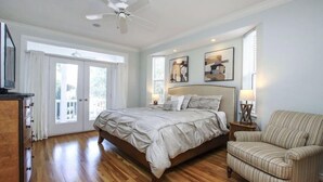 A bedroom with a large bed, a chair, a ceiling fan, and artwork on the walls. - All Seasons Villa (Captiva)