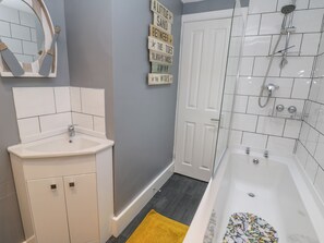 A bathroom with a white sink, a bathtub, and a shower. There is a mirror above the sink and a door with a sign on the wall.