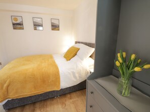 A bedroom with a bed, a bedside table with a vase of tulips, and three framed pictures on the wall.