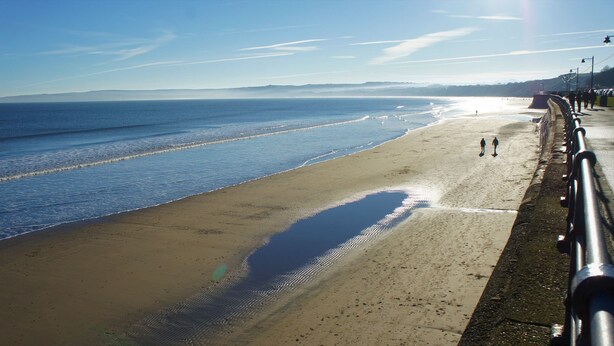 A beach with a concrete walkway and a metal railing. - Sea Glass (Filey)
