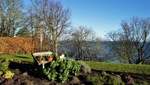 A garden with a wooden bench and potted plants, surrounded by leafless trees and a hedge. - Sea Glass (Filey)