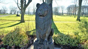 A wooden sculpture of a lion's head mounted on a post in a park. - Sea Glass (Filey)