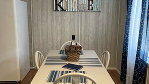 Ein Essbereich mit einem Holztisch, weißen Stühlen, einem gewobenen Korb und einem Schild mit der Aufschrift 'Kitchen' an der Wand.