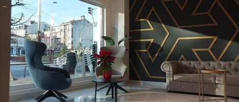 Un intérieur moderne avec une grande fenêtre, un motif géométrique sur le mur et un coin salon comprenant un canapé capitonné et un fauteuil bleu.