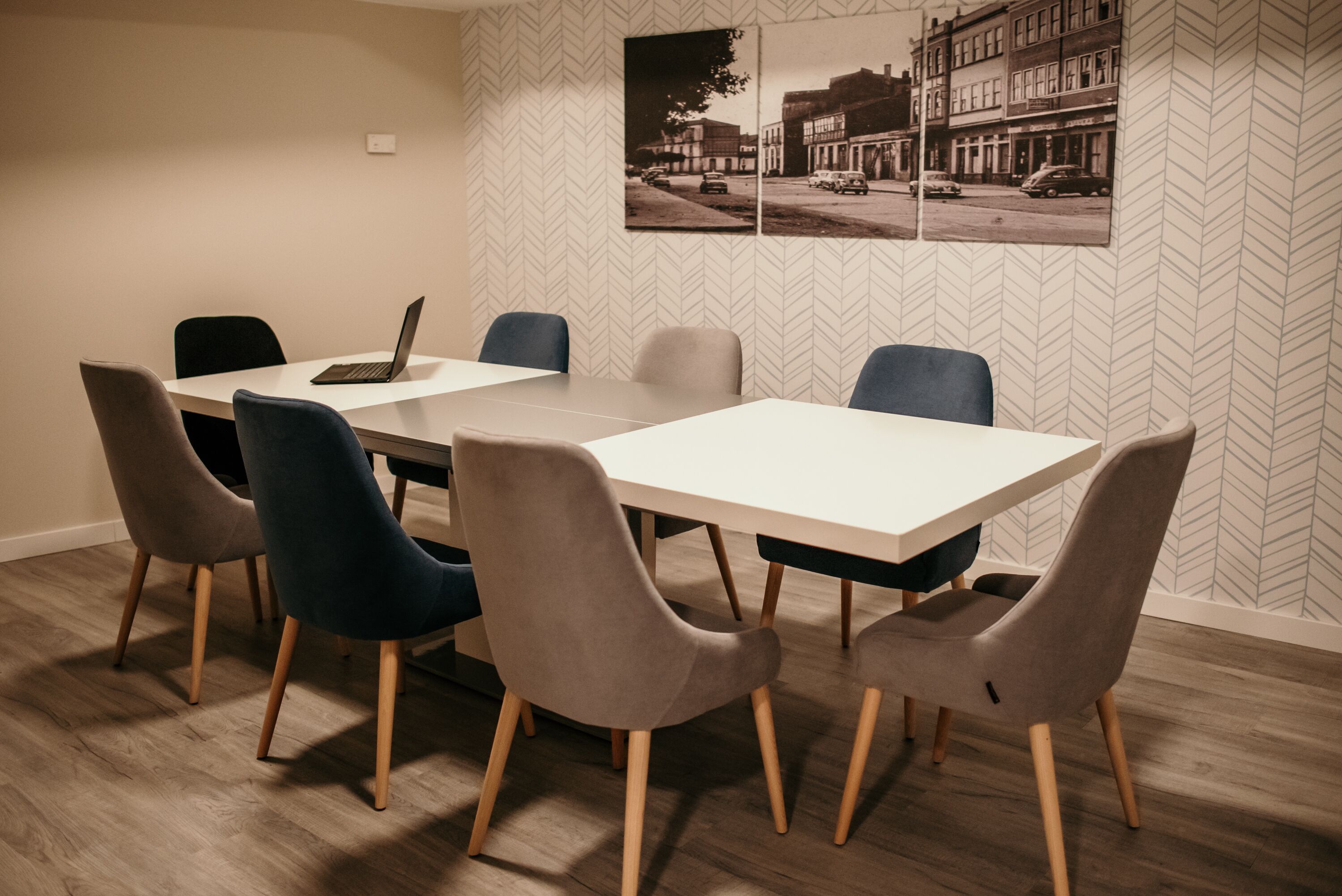 Une salle de conférence avec une table blanche, six chaises et un ordinateur portable.