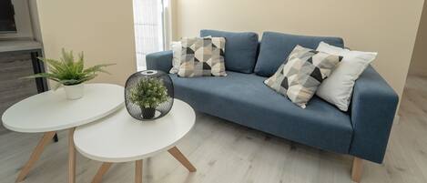 A modern living room with a blue sofa, two white round tables, a potted plant, and a decorative mirror on the wall.