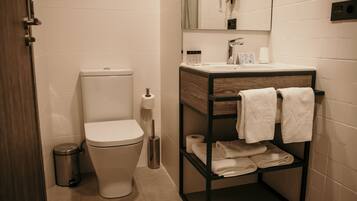 A modern bathroom with a toilet, a sink, a mirror, and a shelf with towels.