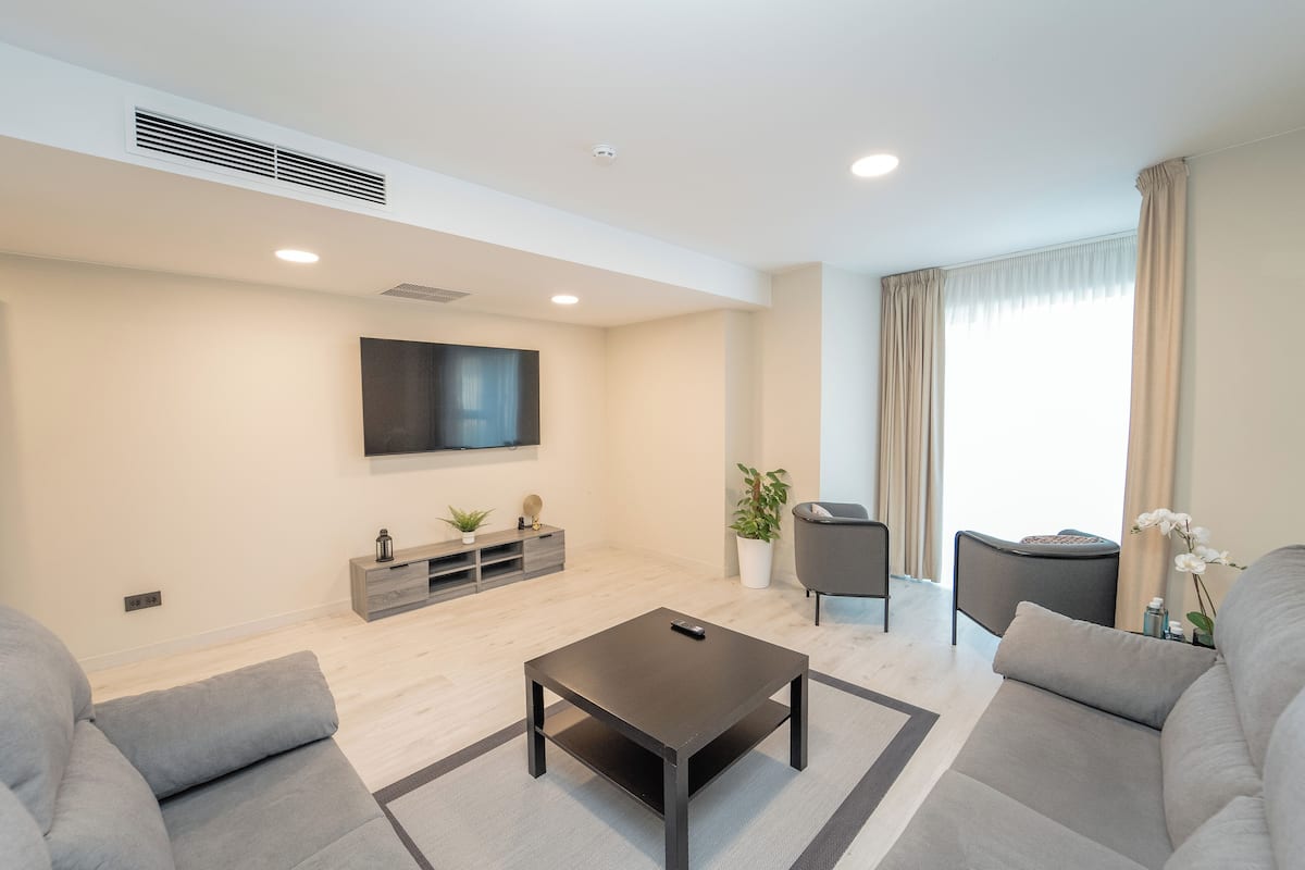 Ein modernes Wohnzimmer mit Fernseher, grauen Sofas, einem Couchtisch und einer Topfpflanze.