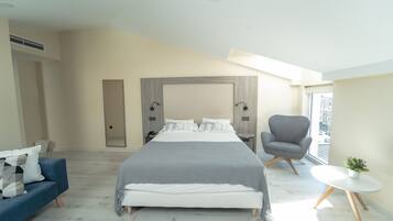 Un dormitorio moderno con una cama grande, un sofá azul, un sillón gris y una pequeña mesa con una planta.