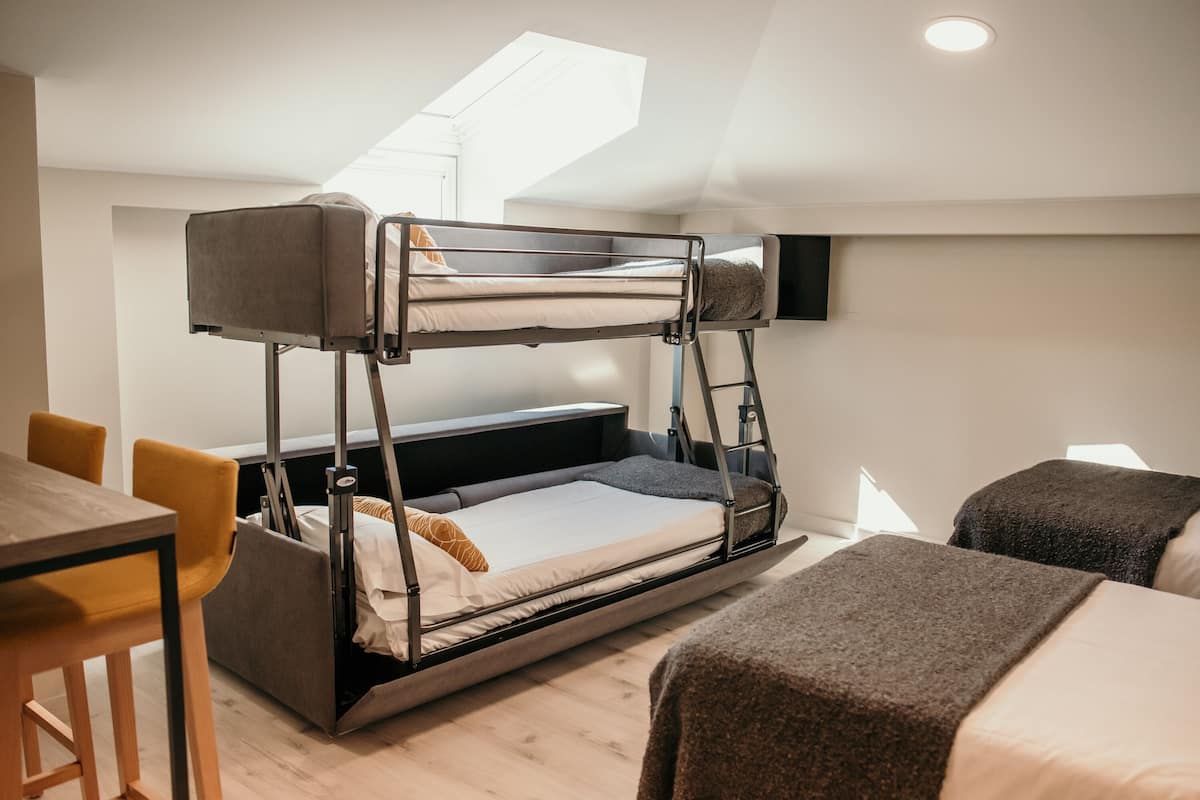 Ein Etagenbett mit Schreibtisch und Stühlen, einem Dachfenster und einem Fernseher an der Wand.