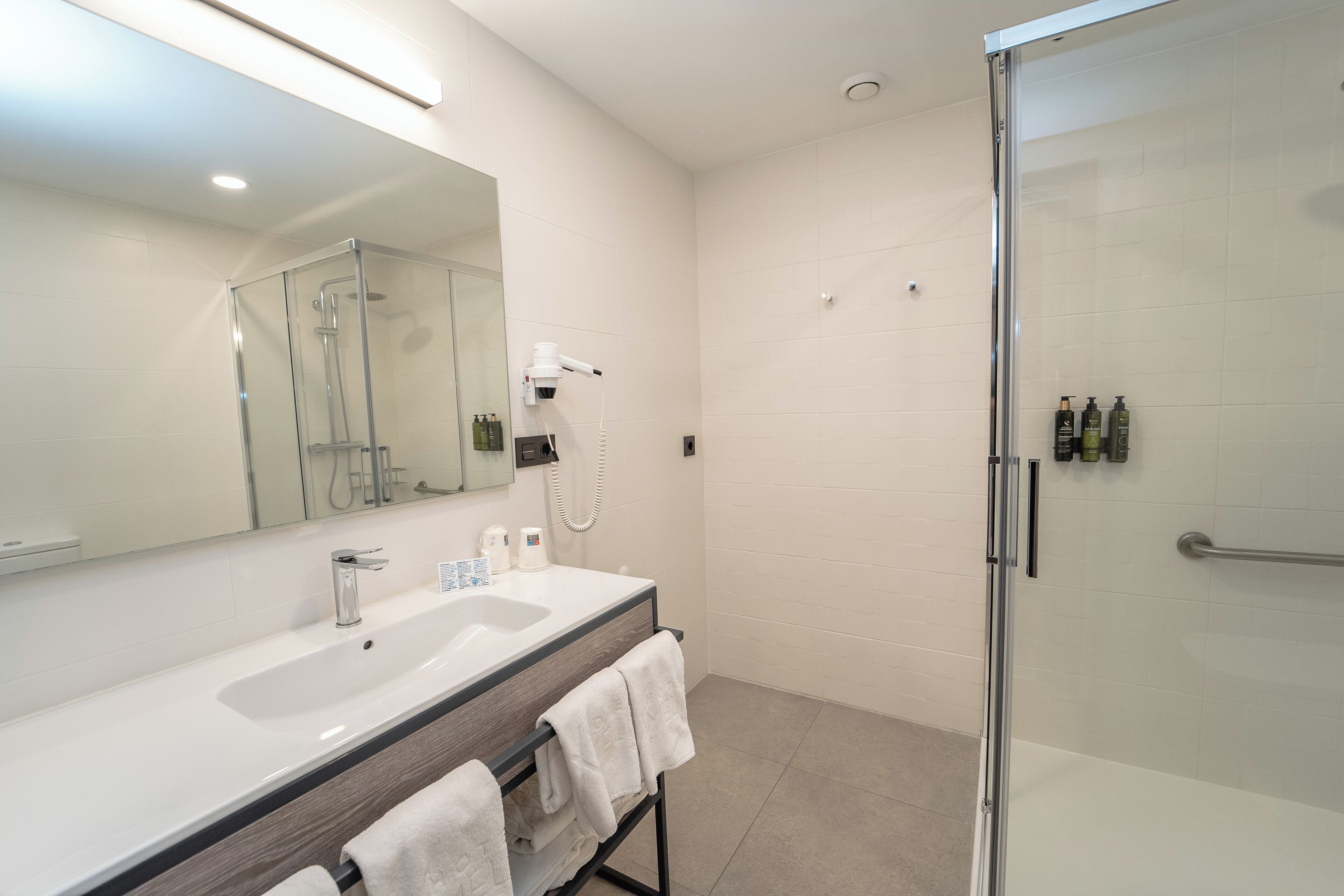 A modern bathroom with a glass shower enclosure, a large mirror, and a vanity with a sink and towel rack.