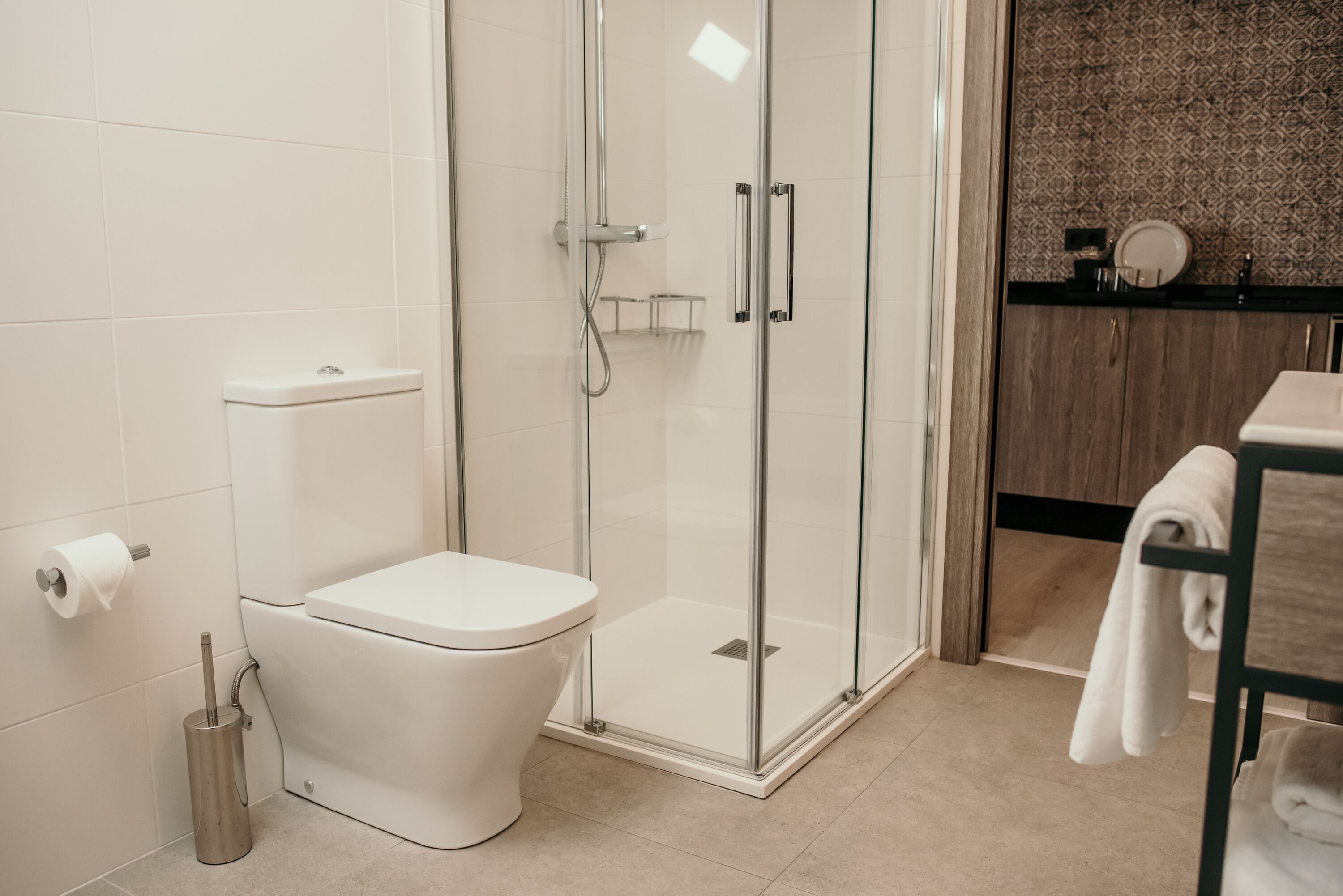 A modern bathroom with a glass-enclosed shower, a white toilet, and a sink with a towel rack.