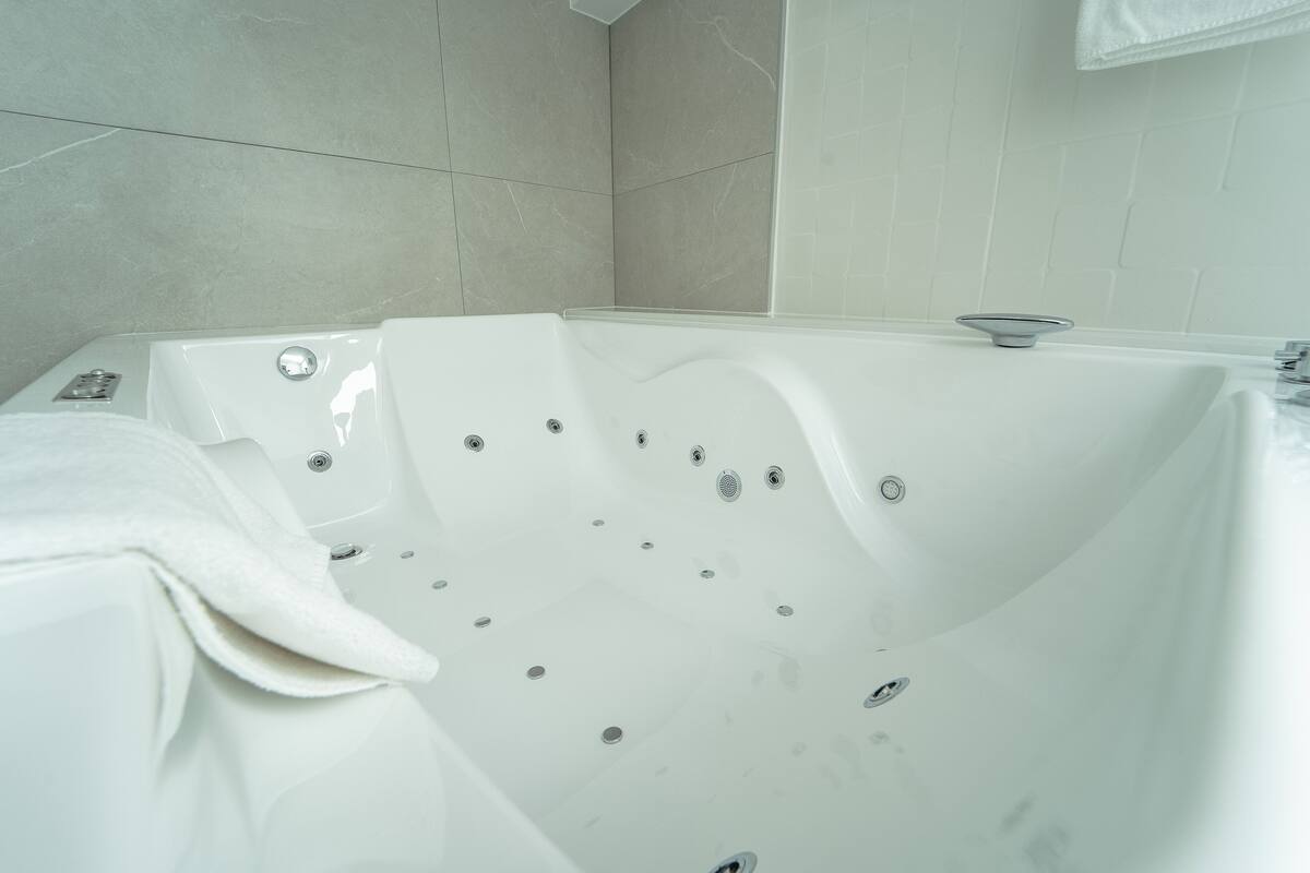 Ein modernes Badezimmer mit einer großen weißen Badewanne, einem sichtbaren Abfluss und einem Handtuchhalter.