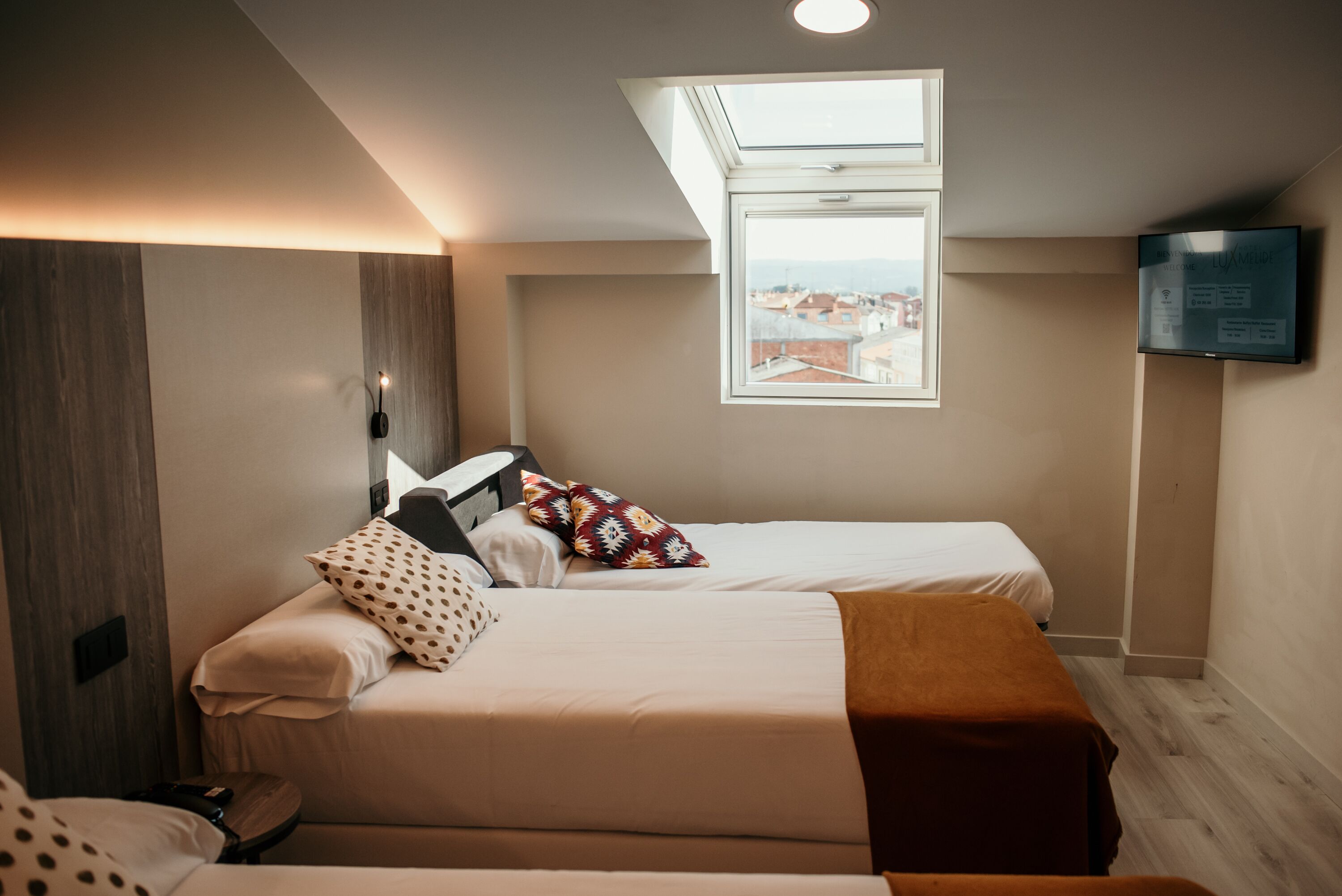 Un dormitorio con dos camas, un tragaluz, televisión y vistas a la ciudad.