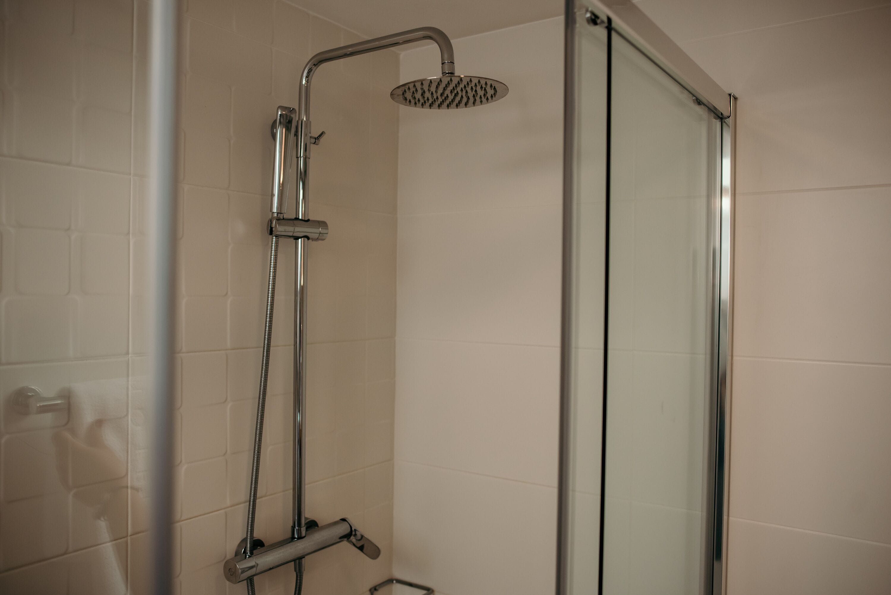 Ducha con puerta de cristal, cabezal de ducha de mano y grifo empotrado.
