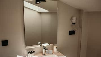 Un baño moderno con un espejo grande, un lavamanos, un secador de pelo y artículos de aseo en la encimera.