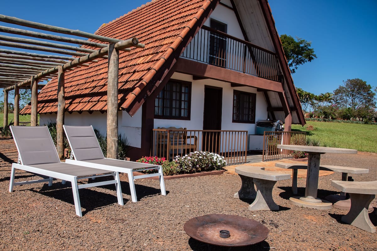 A two-story building with a red-tiled roof, a balcony, and a patio area with a table and chairs.