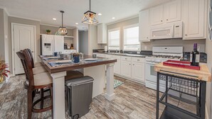 A modern kitchen with white cabinets, a wooden island, a stainless steel refrigerator, and a built-in oven.