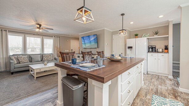 A spacious living area with a large sofa, a dining table, and a kitchen with white cabinets and a wooden countertop.