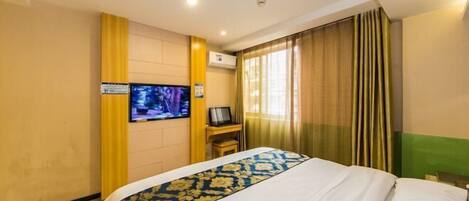 Habitación de hotel con cama, televisor, escritorio y ventana con cortinas.