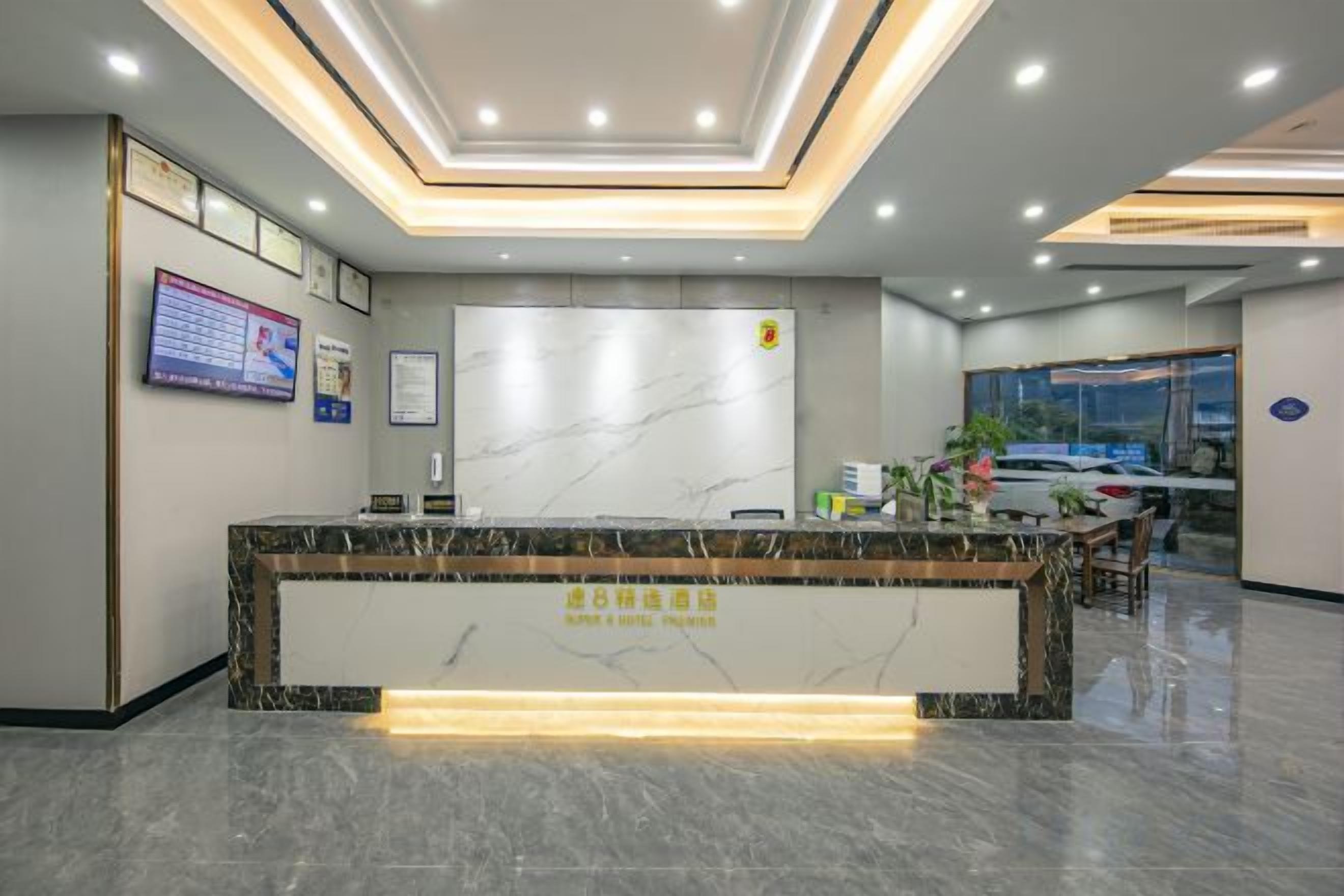 Zona de recepción de un hotel con mostrador de mármol, certificados enmarcados y una pantalla digital.
