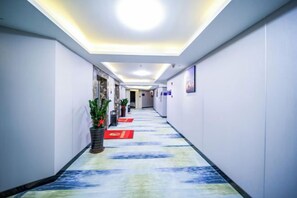A hotel corridor with a patterned carpet, a potted plant, and red signage on the floor. - Super 8 Selected Hotel (Fuzhou IKEA Shangyang Metro Station Branch) (Fuzhou)