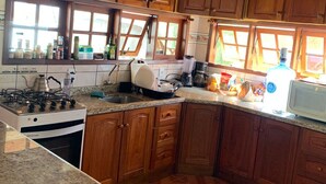 A kitchen with wooden cabinets, a gas stove, a microwave, and a window with a view. - Paradise on the shores of Ibiraquera Lagoon (Imbituba)