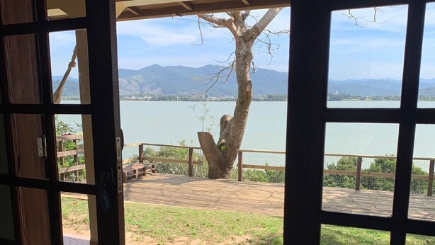 A wooden door leading to a covered outdoor area with a view of a lake and mountains. - Paradise on the shores of Ibiraquera Lagoon (Imbituba)