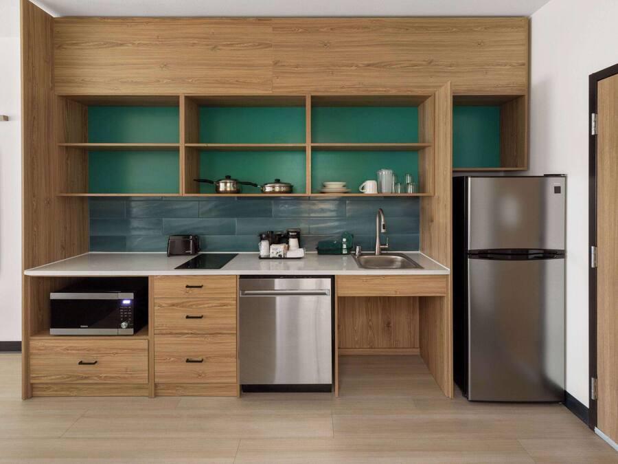 A modern kitchen with wooden cabinetry, a built-in microwave, a dishwasher, and a stainless steel refrigerator.
