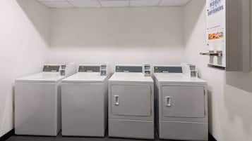 Una sala de lavandería con cuatro lavadoras de carga frontal y un dispensador de detergente, lejía y suavizante.