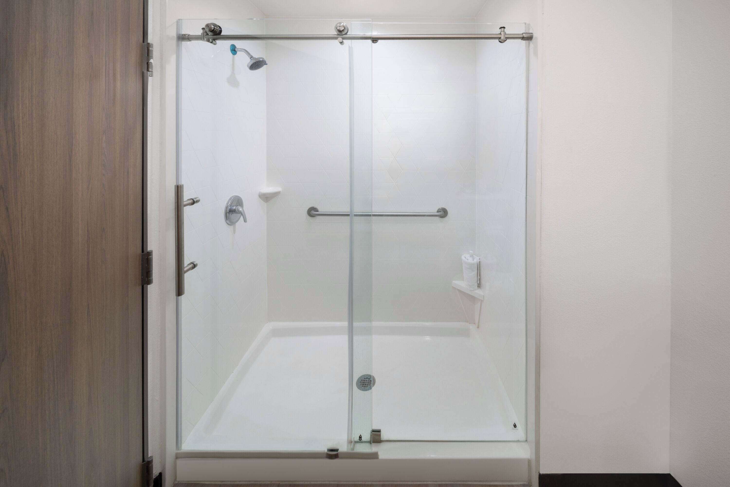 A glass-enclosed shower with a white tiled wall, a metal handle, and a small shelf.