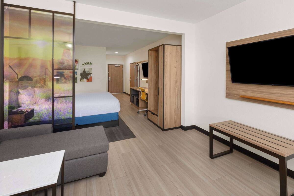 Ein modernes Hotelzimmer mit Bett, einer Couch, einem Schreibtisch, einem Fernseher und einem Kleiderschrank.