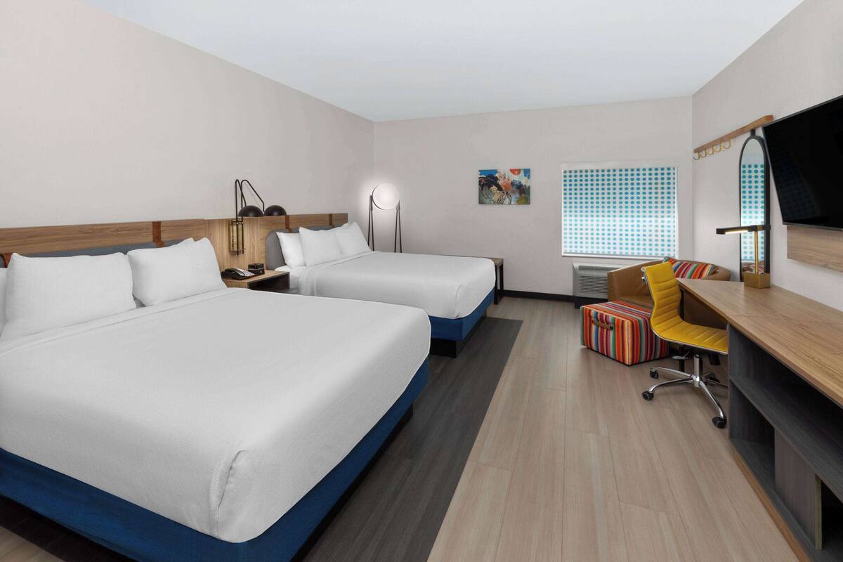 Ein Hotelzimmer mit zwei Betten, einem Schreibtisch mit Stuhl, einem Fernseher und einem Fenster mit Jalousien.