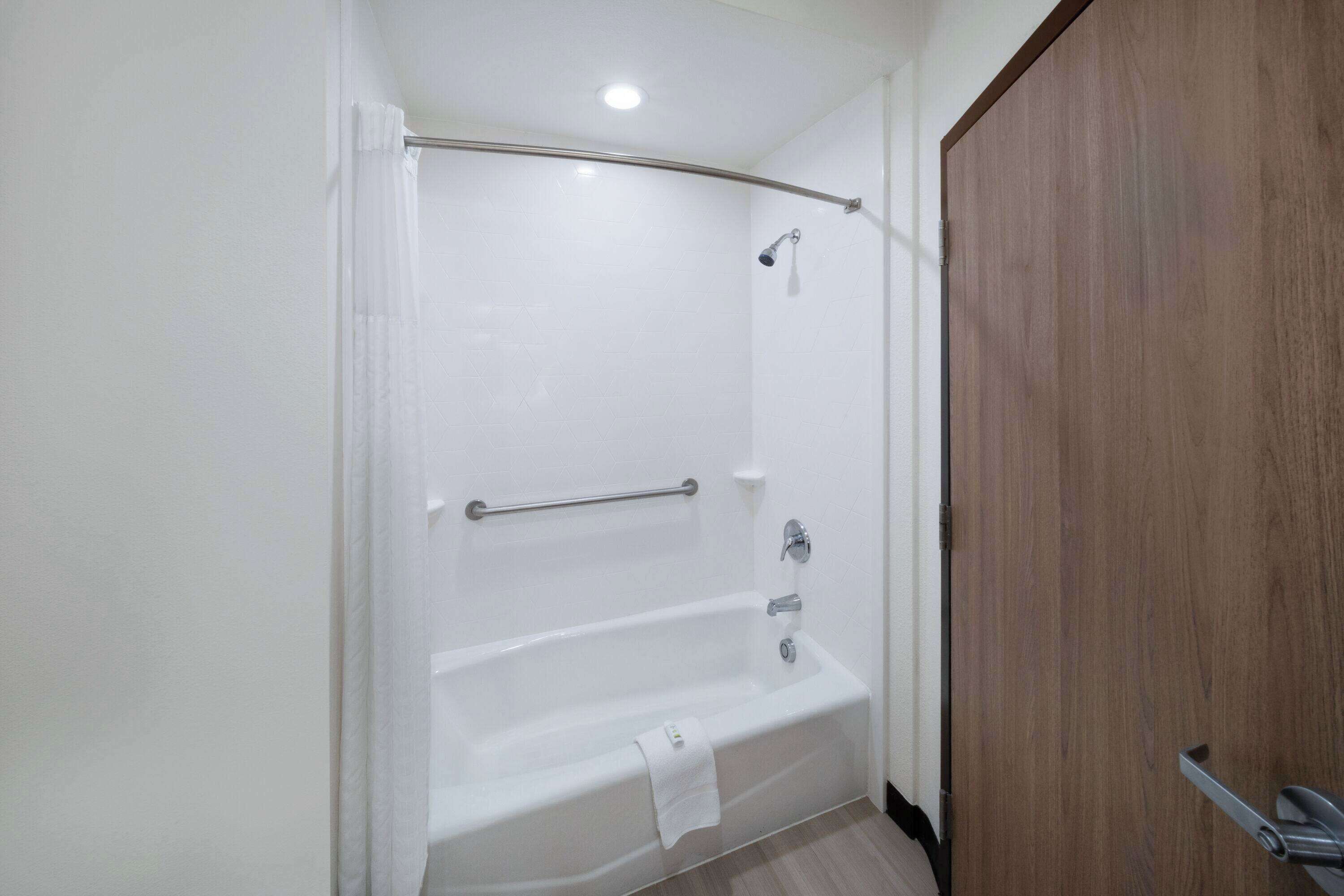 Ein modernes Badezimmer mit einer weißen Badewanne, einer Duschkabine und einer Holztür.