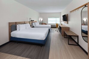 Une chambre d’hôtel avec deux lits, un bureau, une chaise, une télévision, un miroir et une fenêtre avec des stores.