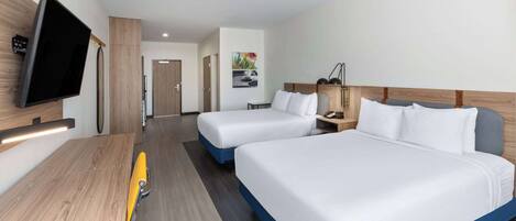 A hotel room with two beds, a desk, a TV, and a bathroom visible in the background.