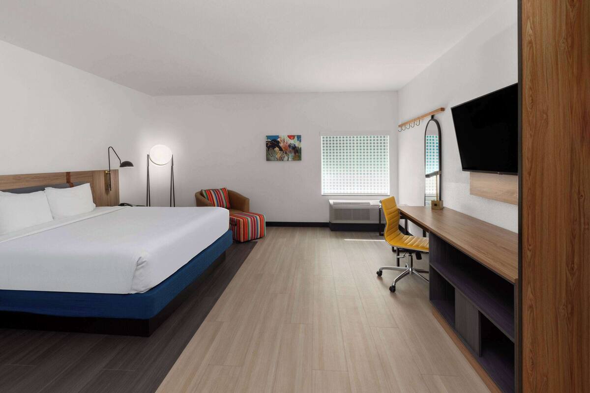 Ein Hotelzimmer mit Bett, Schreibtisch, Stuhl, Fernseher, Bildern und einem Fenster.