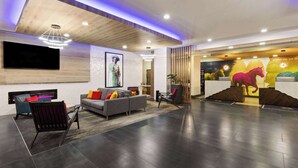 Eine moderne Lobby mit einer Couch, Sesseln, einem Flachbildfernseher und einer Rezeption mit einem Wandgemälde eines Pferdes.