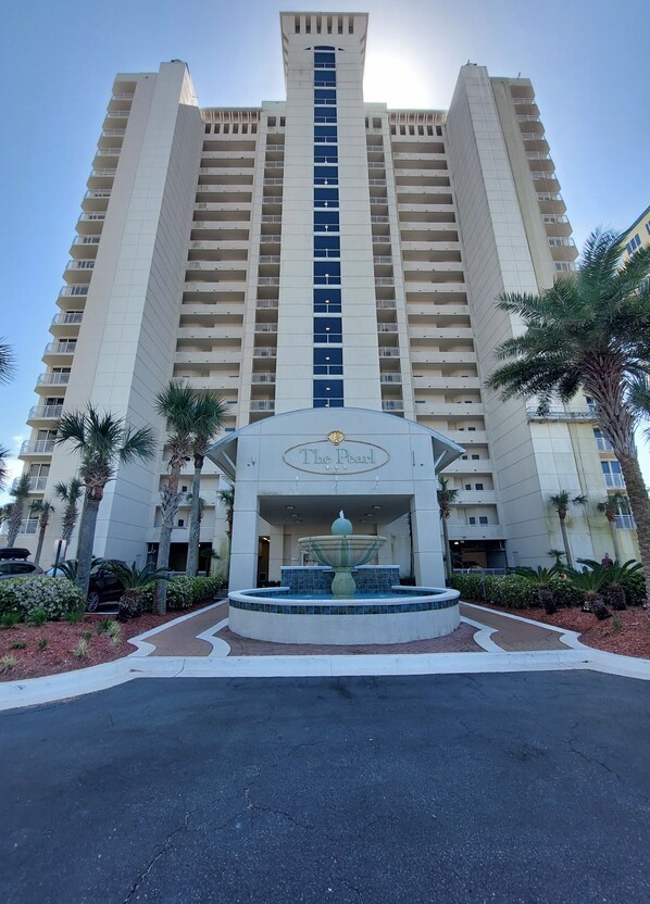 A high-rise hotel with a central fountain, multiple balconies, and palm trees.