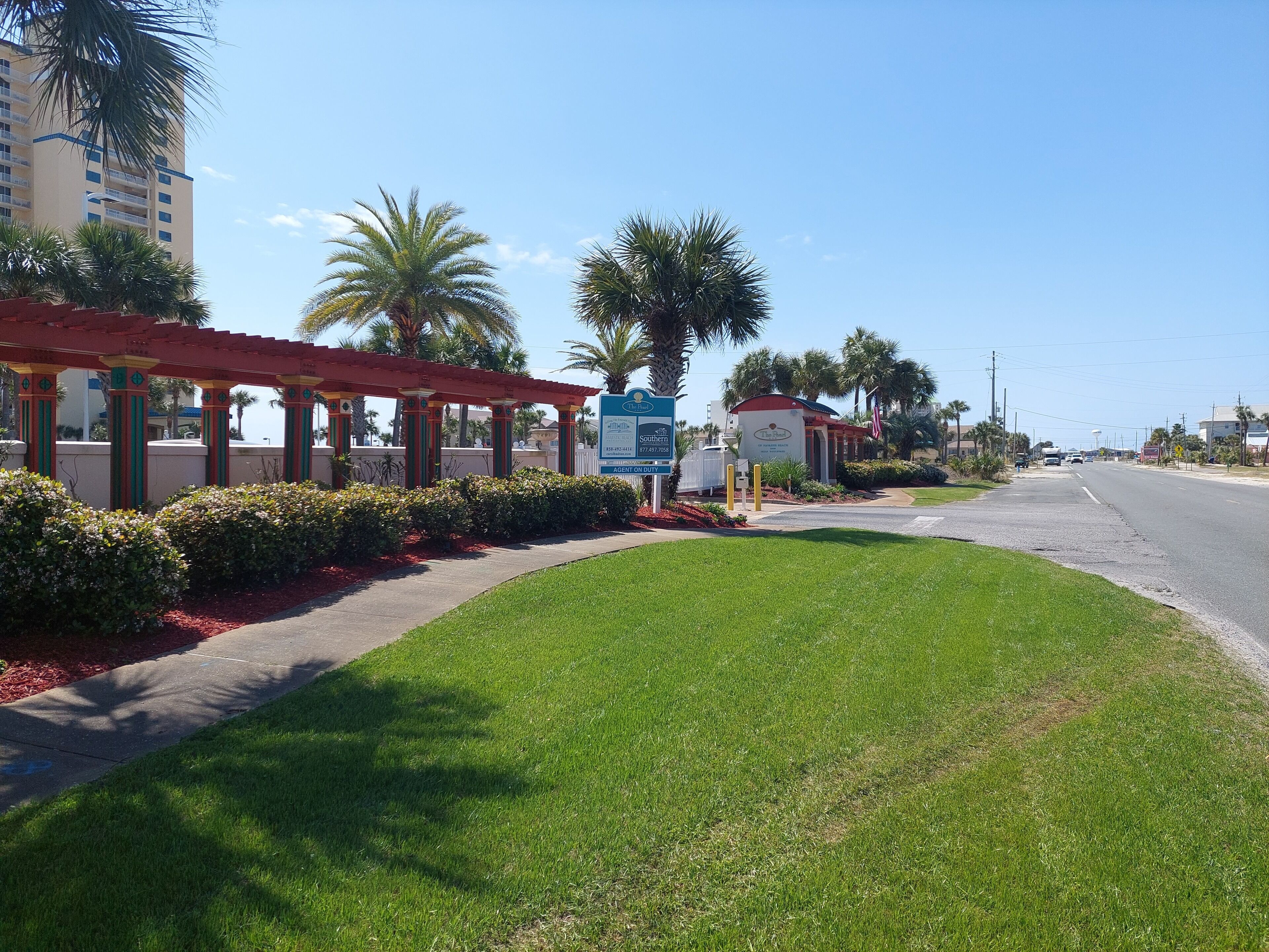 A hotel entrance with a red canopy, palm trees, and a clear sky.