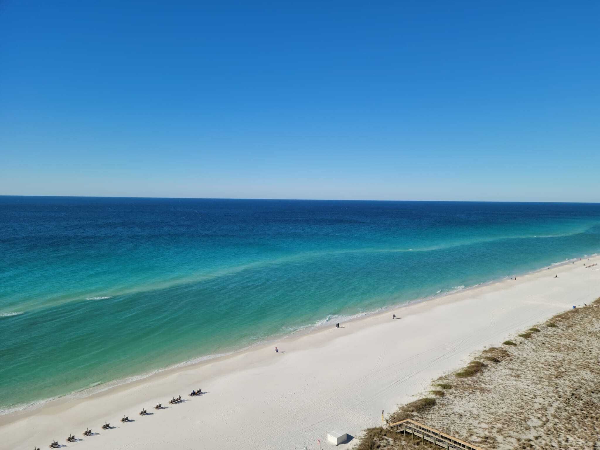 A beach with clear turquoise waters, a sandy shore, and a wooden walkway leading to the water.