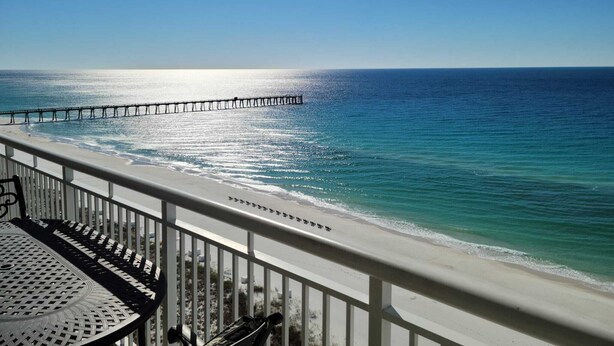 A beach view with a pier extending into the ocean, a white railing, and a metal table. - Stunning Beach Views of Gulf-14th Floor-Dog friendly-See the longest pier in FL! (Navarre)